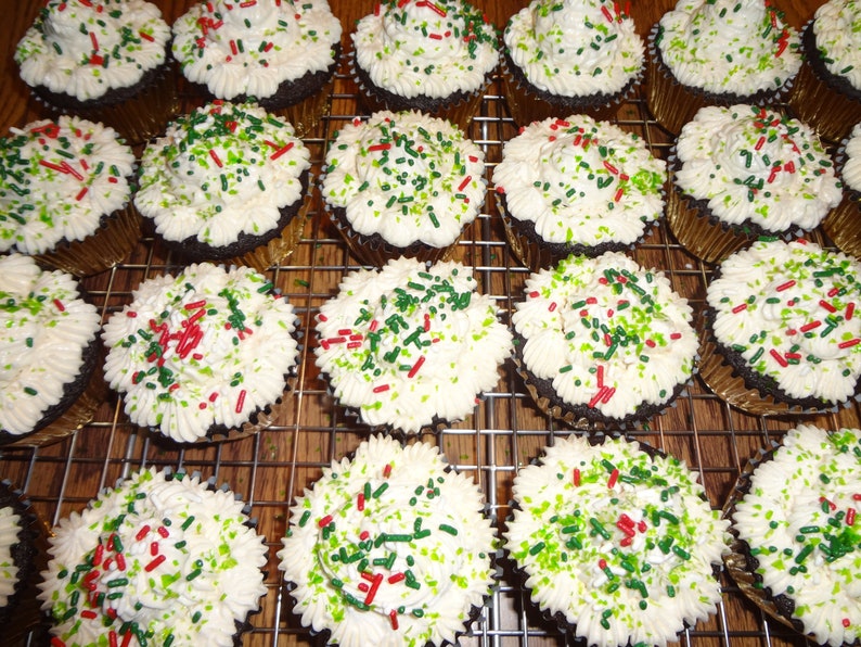 May include: A close-up of a dozen chocolate cupcakes with white icing and green and red sprinkles. The cupcakes are arranged in rows on a wire rack.