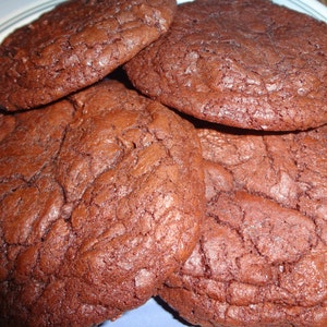May include: Four chocolate chip cookies on a blue and white plate. The cookies are a deep brown color and have a slightly crispy texture.