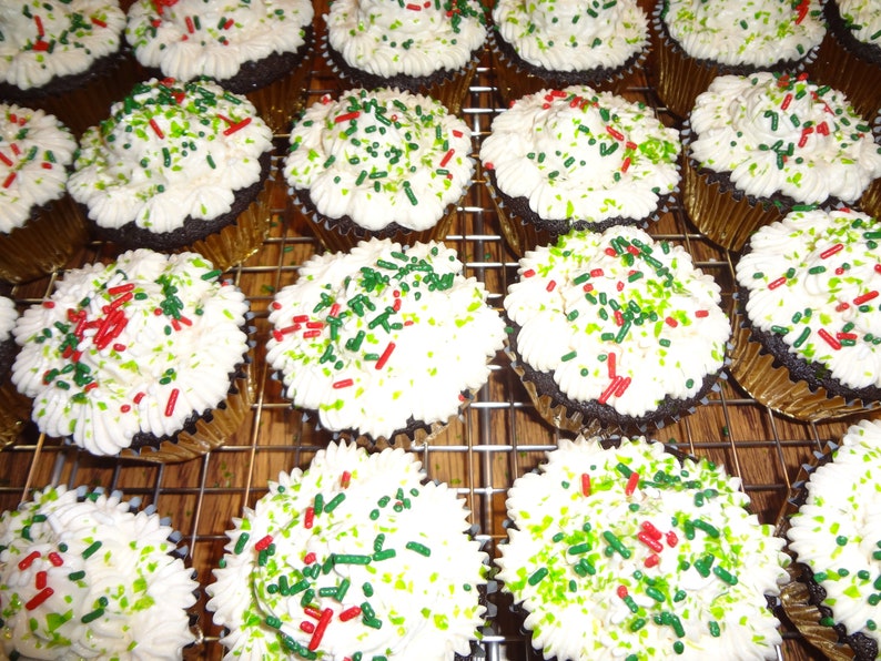 May include: A close-up of a dozen chocolate cupcakes with white icing and green and red sprinkles.