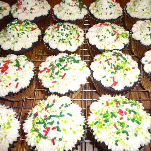 May include: A close-up of a dozen chocolate cupcakes frosted with white icing and decorated with red and green sprinkles.
