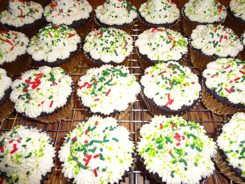 May include: A close-up of a dozen chocolate cupcakes frosted with white icing and decorated with red and green sprinkles.