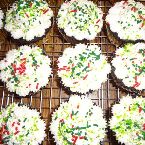 May include: A close-up of a dozen chocolate cupcakes frosted with white icing and decorated with green and red sprinkles.