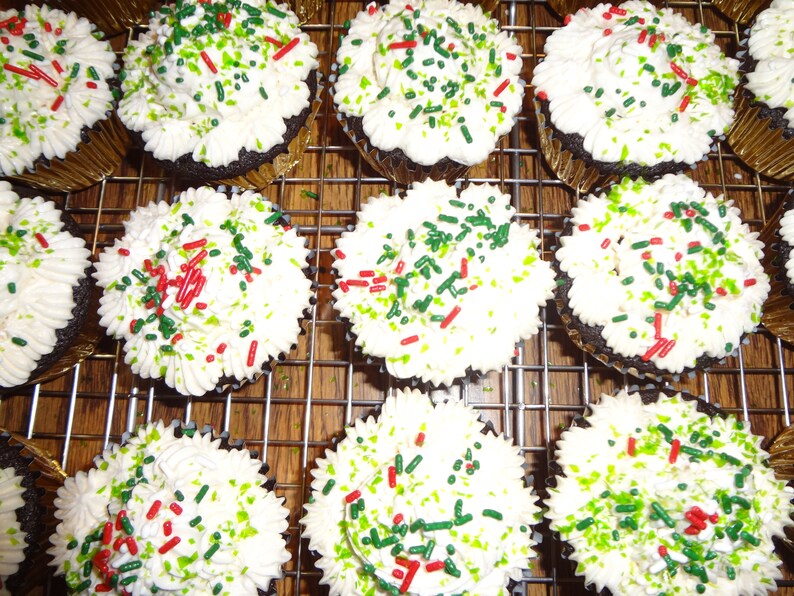 May include: A close-up of a dozen chocolate cupcakes frosted with white icing and decorated with green and red sprinkles.