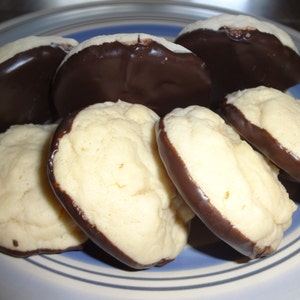 May include: A plate of homemade cookies with a chocolate coating. The cookies are round and have a light brown color. The chocolate coating is dark brown and covers the bottom half of each cookie.
