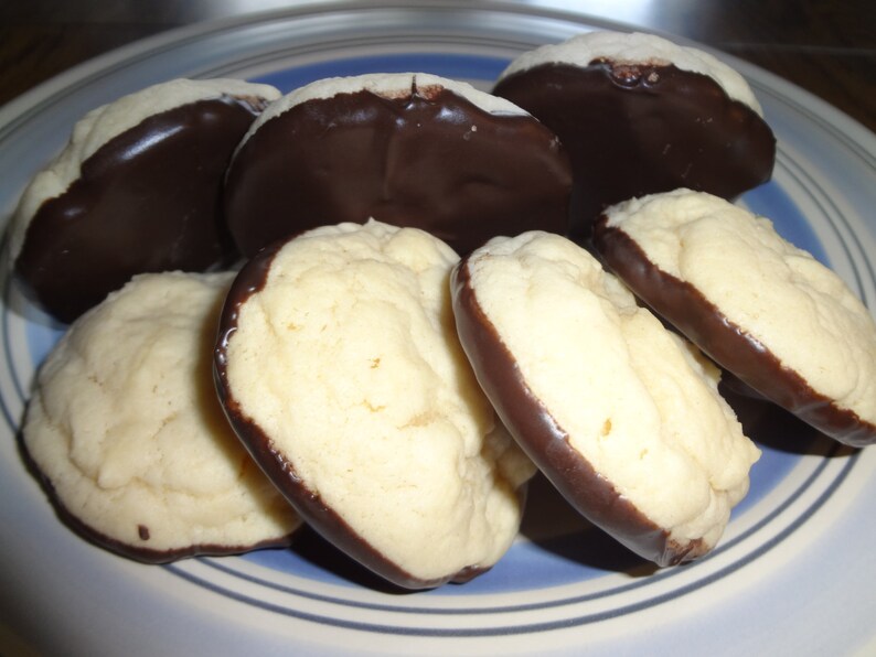 May include: A plate of homemade cookies with a chocolate coating. The cookies are round and have a light brown color. The chocolate coating is dark brown and covers the bottom half of each cookie.