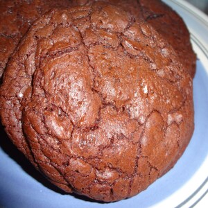May include: Close-up of three chocolate chip cookies on a blue and white plate. The cookies are dark brown and have a slightly cracked surface.