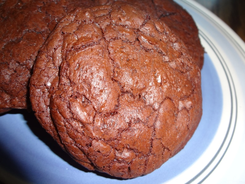 May include: Close-up of three chocolate chip cookies on a blue and white plate. The cookies are dark brown and have a slightly cracked surface.