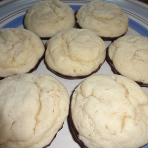 May include: A plate of seven round, white cookies with a dark chocolate coating on the bottom. The cookies are arranged in a circle on a blue and white striped plate.