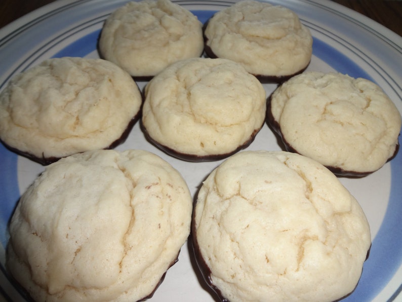 May include: A plate of seven round, white cookies with a dark chocolate coating on the bottom. The cookies are arranged in a circle on a blue and white striped plate.