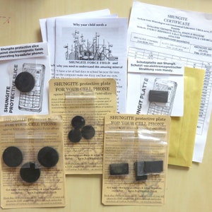 May include: Three small packages containing black shungite protective plates for cell phones. Each package has a label that reads "Shungite protective plate for your cell phone against EMF (Electro Magnetic Field) effects".