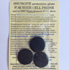 May include: A white card with black text and three black round stickers. The text reads "Shungite protective plate for your cell phone against EMF (Electro Magnetic Field) effects".
