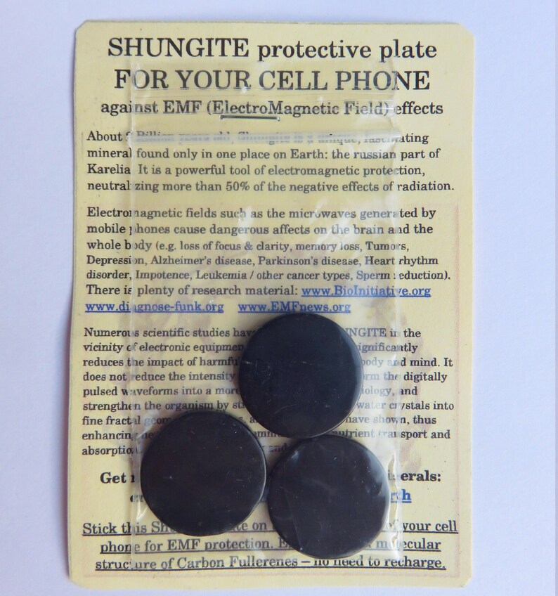 May include: A white card with black text and three black round stickers. The text reads "Shungite protective plate for your cell phone against EMF (Electro Magnetic Field) effects".