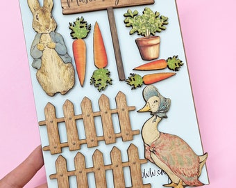 Pode incluir: Uma placa de madeira azul clara com o tema Peter Rabbit. Inclui um letreiro que diz "Mason's Garden", um coelho, um pato, cenouras, uma cerca e uma planta em vaso. As peças de madeira são intrincadamente cortadas e pintadas.