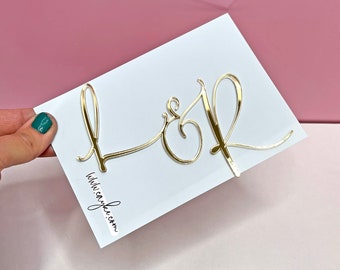 May include: A white card with gold foil letters spelling "L & R" and the text "withlovejake.com" printed in black.