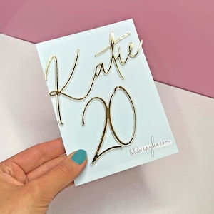 May include: A white card with gold foil lettering that says "Katie 20" and a website address at the bottom.