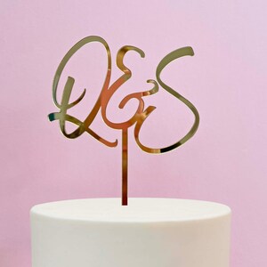 May include: Gold mirrored cake topper with the word "&" in a cursive script.