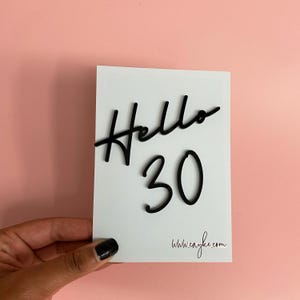 May include: White card with black lettering that says "Hello 30" and a website address at the bottom.