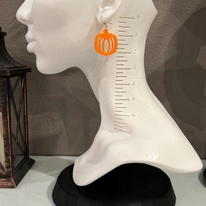 May include: Orange pumpkin-shaped dangle earrings on a white mannequin head. The earrings are about 1.5 inches long.