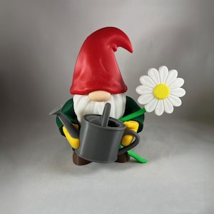 May include: A garden gnome figurine with a red hat, white beard, and green jacket. The gnome holds a gray watering can in one hand and a large white daisy with a yellow center in the other. The gnome's gloves are yellow.