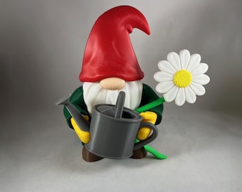 Può includere: Statuetta di gnomo da giardino con cappello rosso, barba bianca e giacca verde. Lo gnomo tiene in mano un annaffiatoio grigio e una grande margherita bianca con centro giallo. I guanti dello gnomo sono gialli.