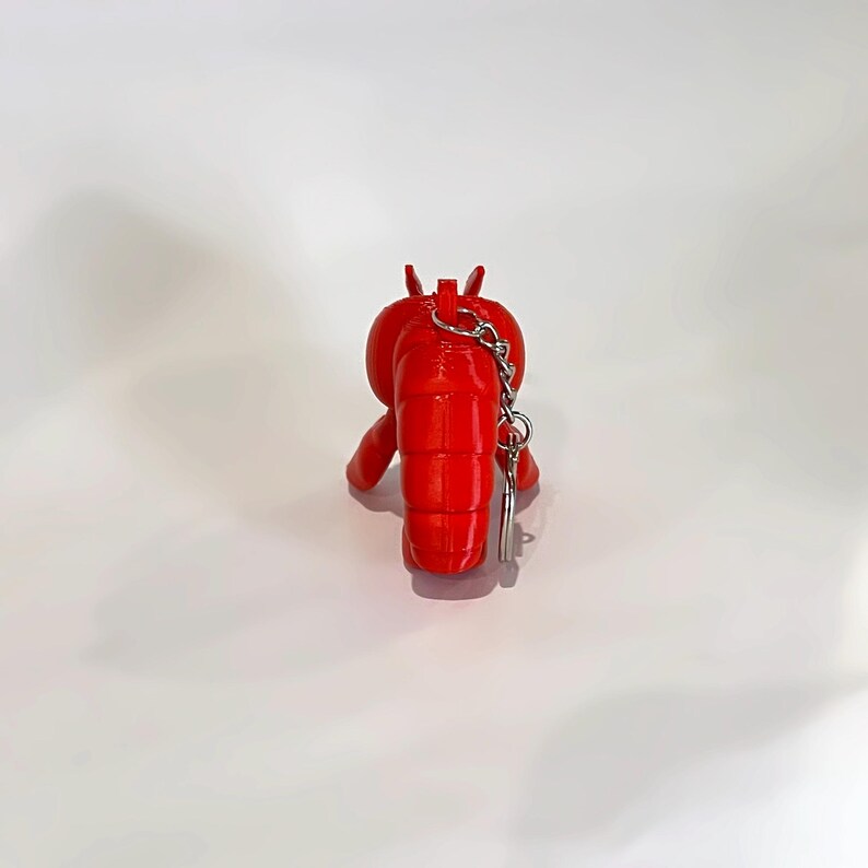 May include: A vibrant red lobster keyring. The lobster is made of a solid material and has a silver-coloured chain and key ring attached. The lobster is facing away from the camera.