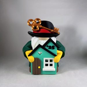 May include: A whimsical figurine of a gnome wearing a black hat with gold-colored keys and a green coat, holding a teal house with the number '25'. The house has a brown door and a white window.