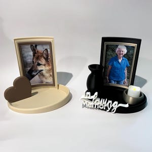 Puede incluir: Dos conjuntos conmemorativos. El conjunto izquierdo es beige con forma de corazón y la foto de un perro. El derecho es negro con un jarrón, una vela blanca, la foto de una persona y el texto blanco In Loving Memory en la base.