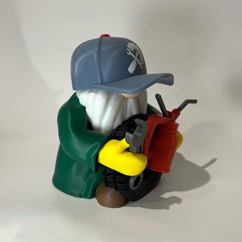 May include: A whimsical figurine of a mechanic gnome. The gnome wears a blue cap with a wrench logo, a green jacket, and yellow gloves. He holds a tire, a wrench, and a red gas can. The gnome has a white beard and a brown base.