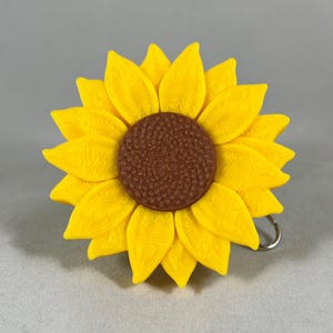 Pode incluir: Um girassol amarelo com um centro marrom. O girassol é feito de plástico e tem uma superfície texturizada.