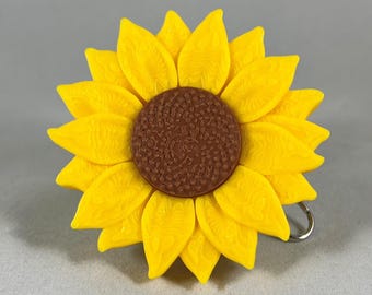May include: A yellow sunflower with a brown centre. The sunflower is made of plastic and has a textured surface.