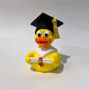 May include: A yellow rubber duck wearing a black graduation cap with a gold tassel and holding a diploma. The duck has a white collar and an orange beak. The duck is a fun, novelty item.