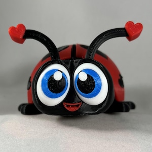 May include: A 3D printed ladybug toy with large blue eyes, a red body, and black antennae with red hearts on the ends.
