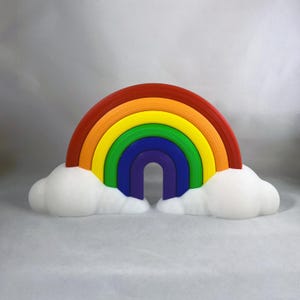May include: A colorful rainbow sculpture with red, orange, yellow, green, blue, and purple arches. The rainbow rests on two fluffy white cloud shapes. The sculpture is a vibrant decorative piece.