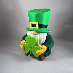 May include: A green leprechaun figurine with a green top hat, black band, and yellow buckle. The gnome wears a green coat, yellow gloves, and holds a green shamrock. The figurine has a white beard and a wooden nose. A festive St. Patrick's Day decoration.