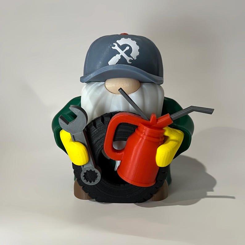 May include: A whimsical gnome figurine dressed as a mechanic, wearing a gray cap with a wrench logo. The gnome holds a gray wrench and a red oil can, with a tire behind it. The gnome has a white beard, yellow gloves, and a green jacket.