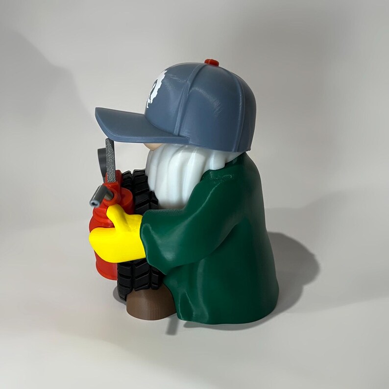 May include: A whimsical figurine of a gnome wearing a blue baseball cap with a white emblem, a green coat, and yellow gloves. The gnome is holding a red and black object, possibly a tool or a piece of equipment.
