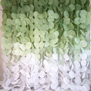 May include: A decorative wall hanging composed of numerous circular paper discs strung together in vertical strands. The discs feature a color gradient transitioning from a deep forest green at the top to a light sage and finally to white at the bottom.