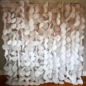 May include: A white and beige ombre paper garland with round paper circles hanging from a copper pipe frame. The garland is made of felt and is perfect for a wedding or party backdrop.