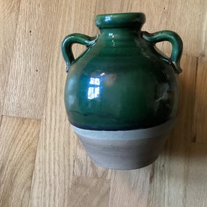 May include: A green ceramic vase with two handles and a white base. The vase has a glossy finish and is decorated with a subtle glaze.
