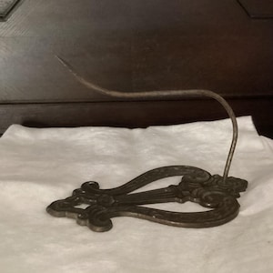 May include: A cast iron hook with a decorative lyre design. The hook is black and has a curved shape. It is designed to be mounted on a wall.