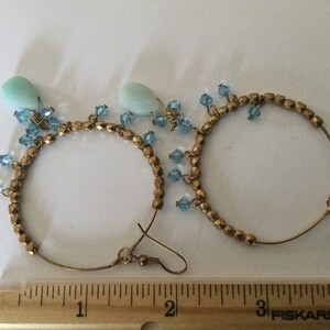 May include: A pair of gold hoop earrings with blue crystal accents and light blue teardrop-shaped stones hanging from the hoops.