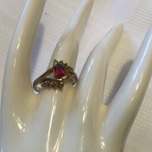 May include: A gold ring with a red gemstone and small clear stones set in a leaf design.