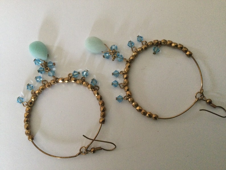 May include: A pair of gold hoop earrings with blue crystal accents and light blue teardrop-shaped stones.