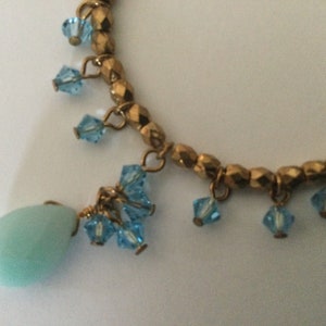 May include: A gold beaded necklace with a light blue teardrop pendant and blue crystal accents.