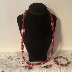 May include: A red and gold beaded necklace, bracelet, and earrings set. The necklace is long and features square-shaped beads with gold accents. The bracelet and earrings are shorter and feature similar beads.