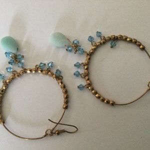 May include: A pair of gold hoop earrings with blue crystal accents and light blue teardrop-shaped stones.