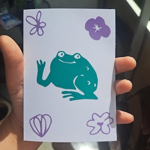 happy little froggo, greeting card with a green frog and purple flowers