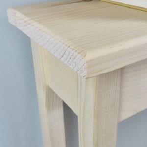 May include: A light wood console table with a simple design. The table has a rectangular top and four legs. The table is made of unfinished wood and has a natural wood grain.