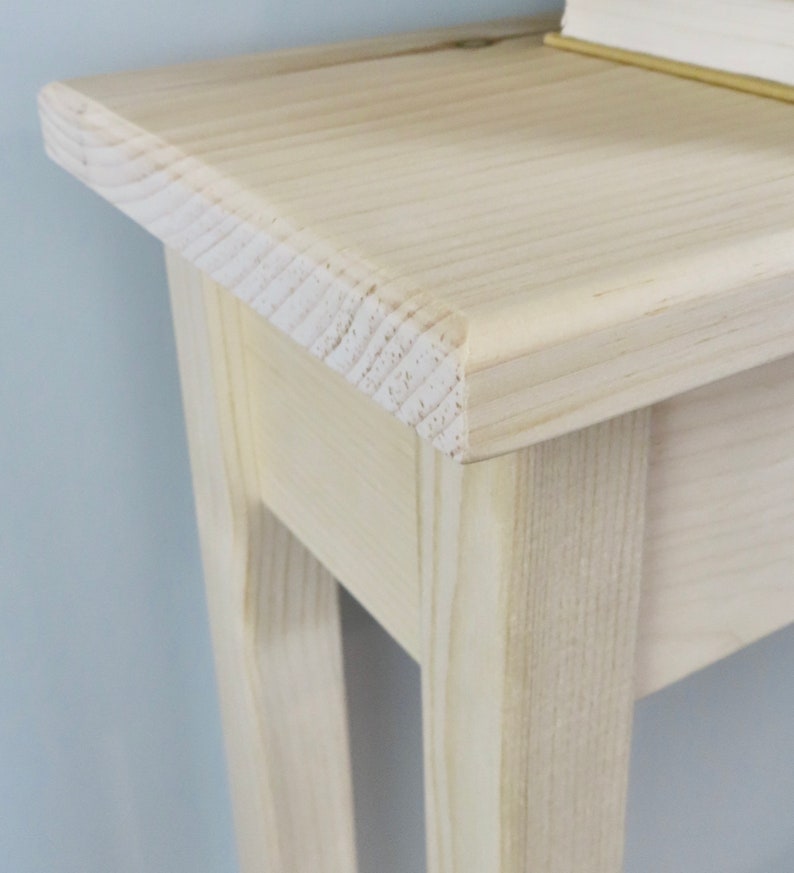 May include: A light wood console table with a simple design. The table has a rectangular top and four legs. The table is made of unfinished wood and has a natural wood grain.