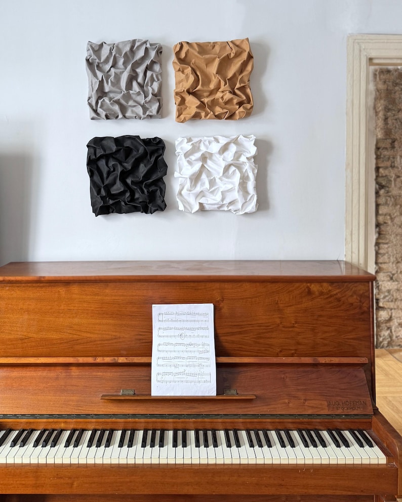 May include: A wooden piano with a sheet of music on the stand, and four square wall art pieces in gray, tan, black, and white. The piano has black and white keys and a polished wood finish.